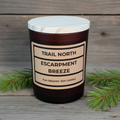 Candle labeled 'Trail North Escarpment Breeze' on a wooden surface
