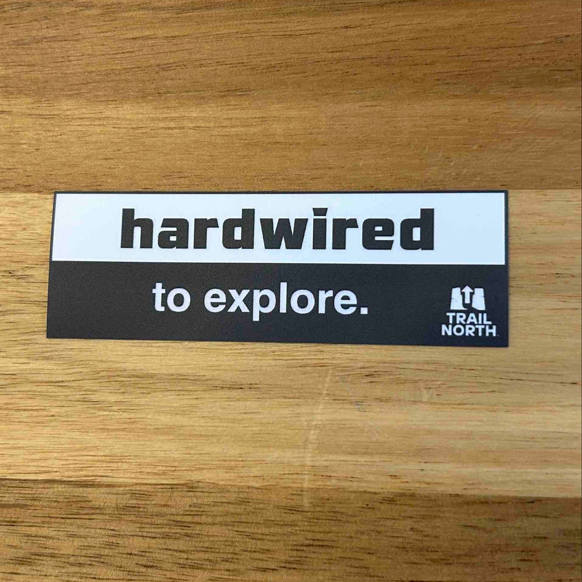 Sticker with 'hardwired to explore.' text on a wooden surface